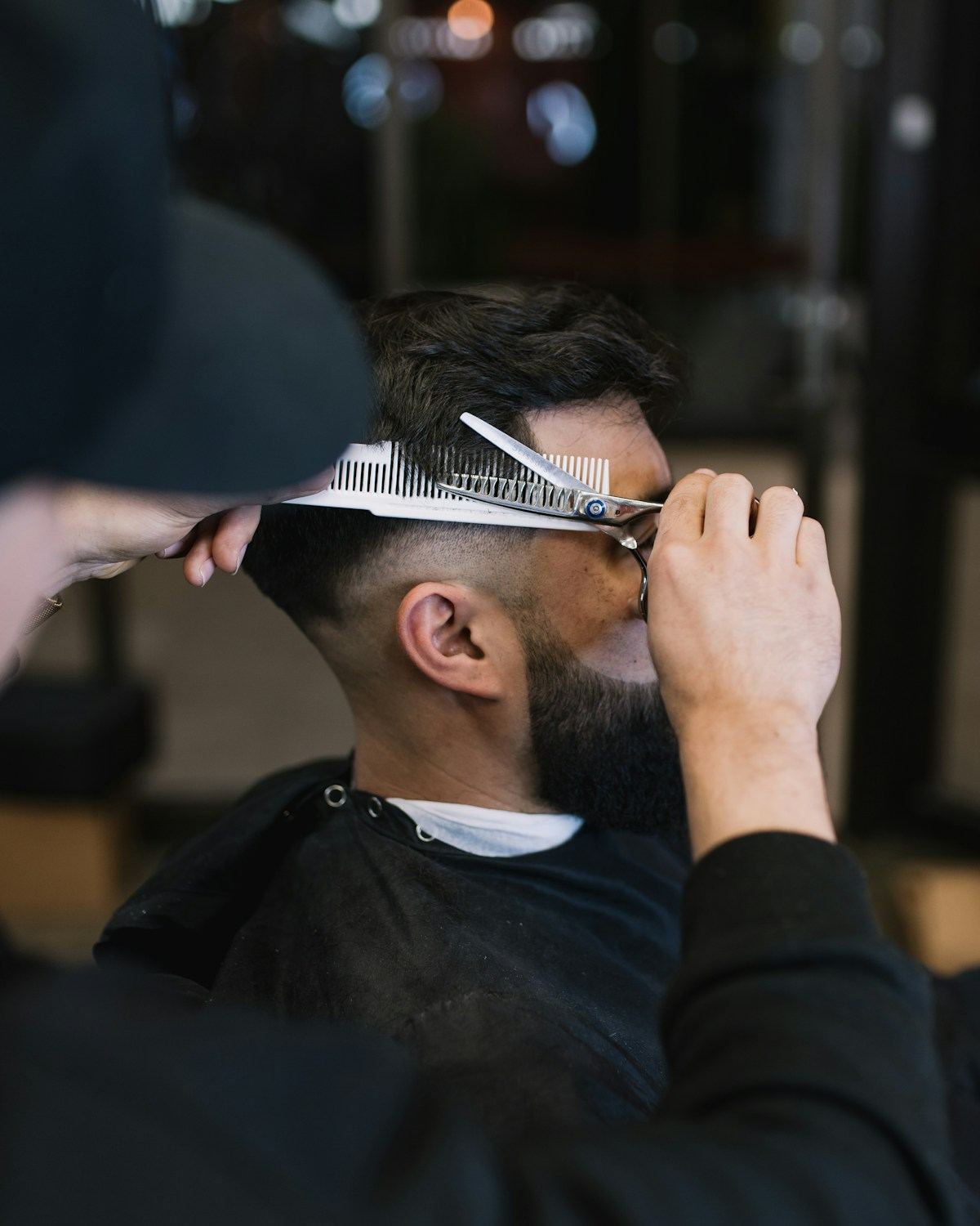 A barber trimming a client's hair with scissors and a comb