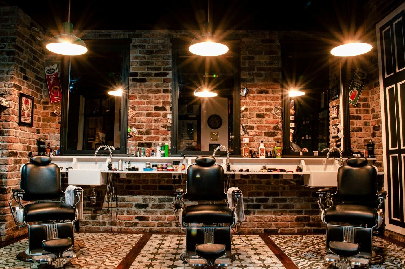 Three leather barber chairs in front of mirrors and a brick wall