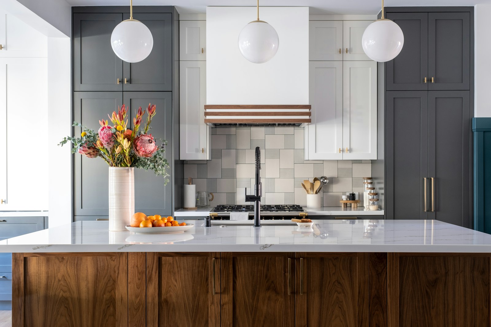A remodeled kitchen with a walnut island, gray cabinets, brass pendant lights and a tiled range wall