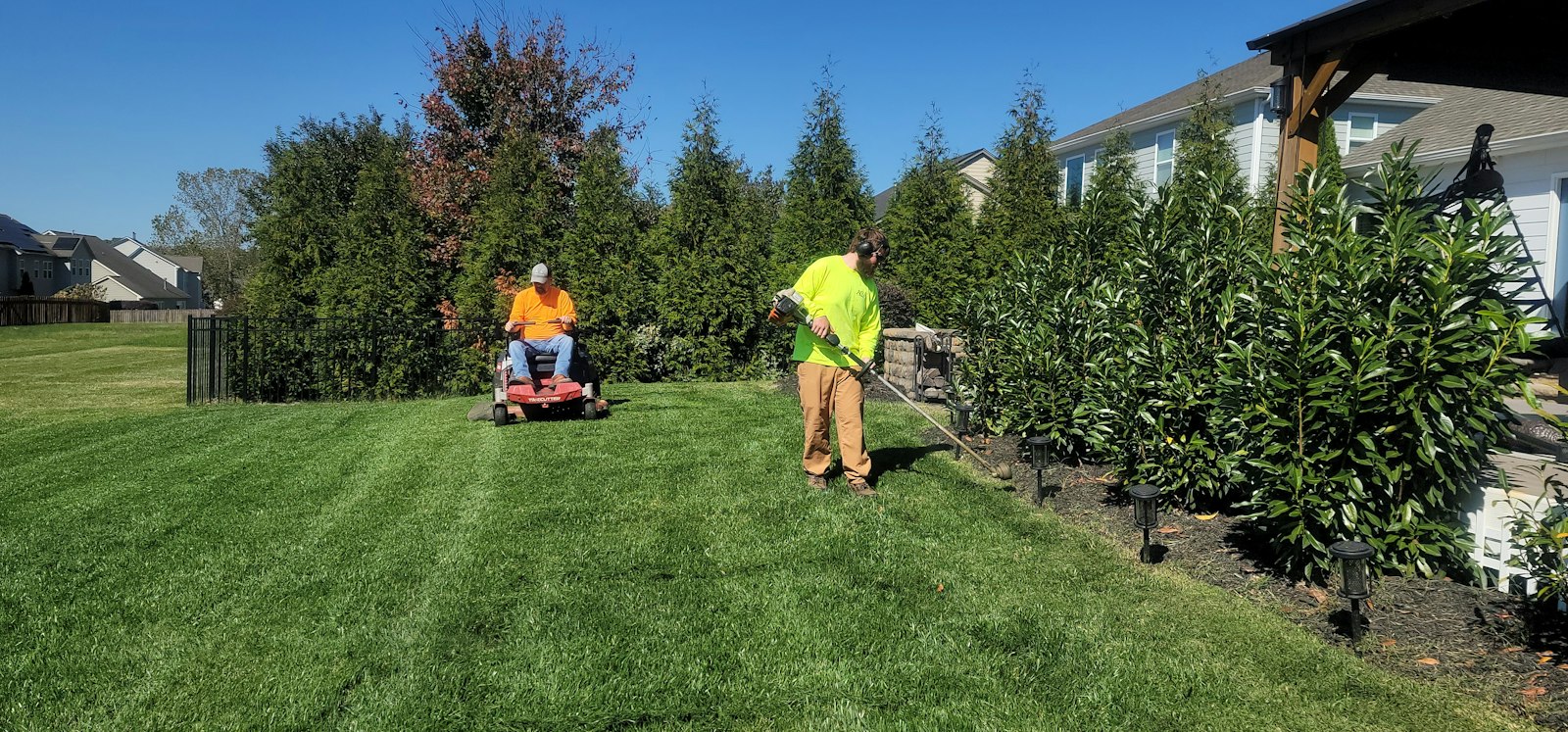 Two Ahtanum crew members mowing and trimming a large residential lawn
