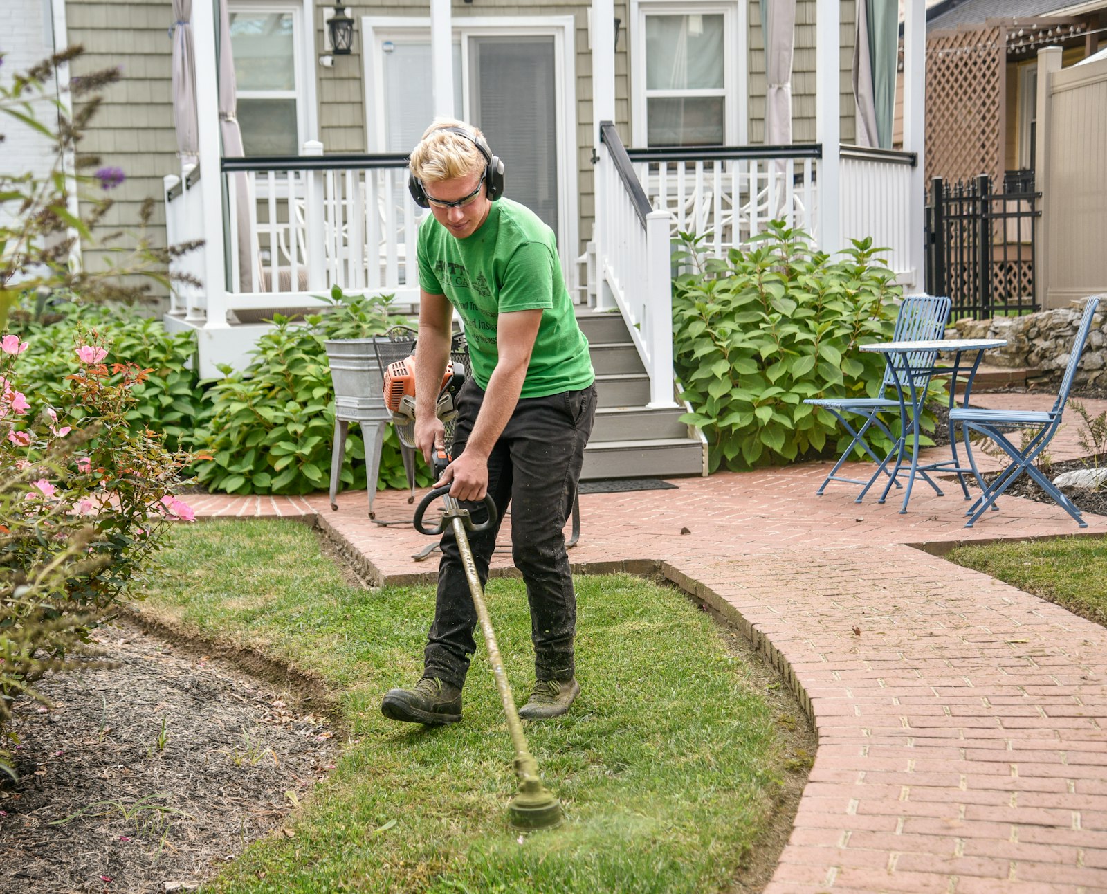 An Ahtanum crew member trimming the lawn edge along a brick path in front of a house
