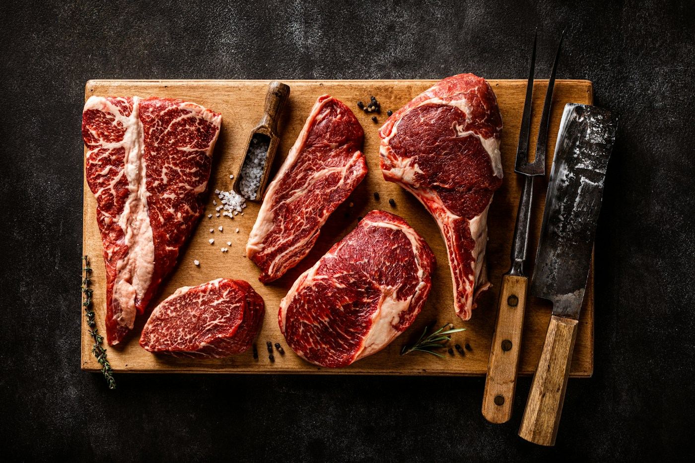 Raw ribeye, strip and filet cuts on a wooden butcher board with knives