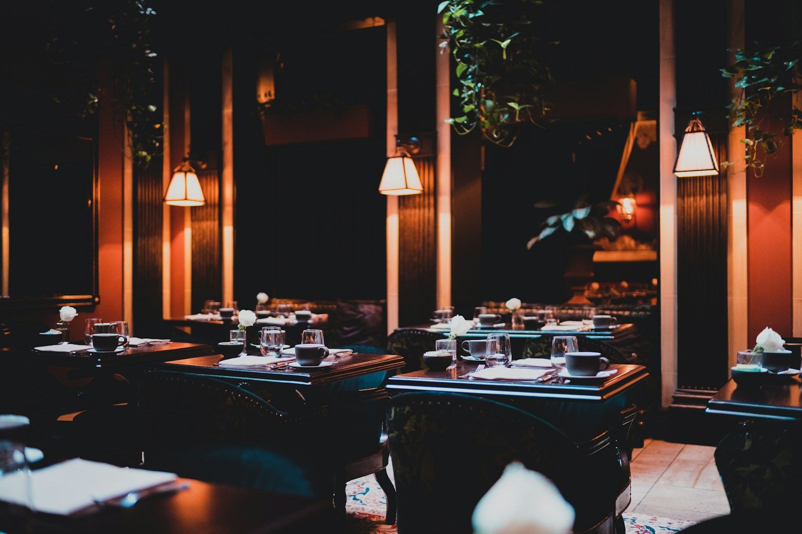 A dimly lit dining room with set tables and warm pendant lights