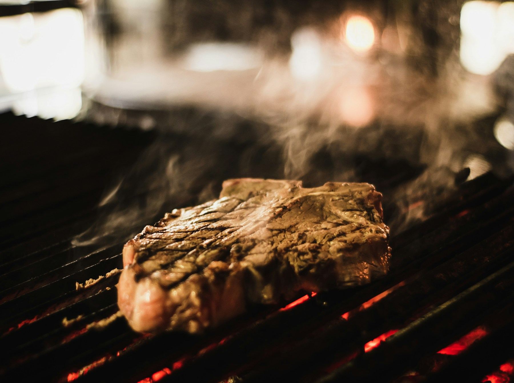 A thick steak searing over a wood fire, smoke rising