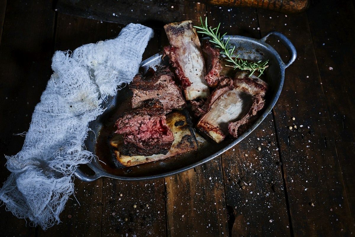 A sliced bone-in tomahawk steak in a cast iron pan with rosemary
